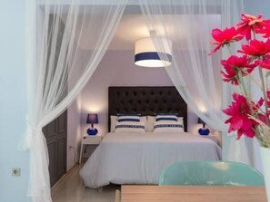 Ein Schlafzimmer mit einem Bett, Nachttischen, einer Lampe, einem Sessel und einer Vase mit Blumen.