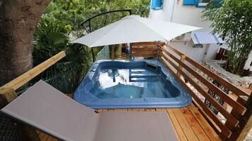 Un bain à remous sur une terrasse en bois, avec une clôture en bois et un arbre à proximité.
