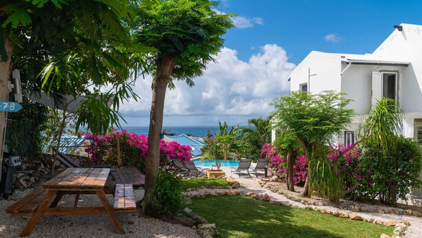 A poolside area with a wooden table, lounge chairs, and a view of the ocean. - Blue Sail Apartments - 1 bedroom apartments (sint maarten)