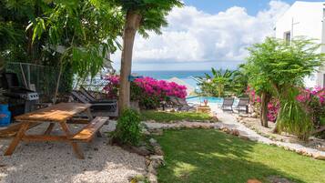 A patio with a grill, lounge chairs, and a view of the ocean.
