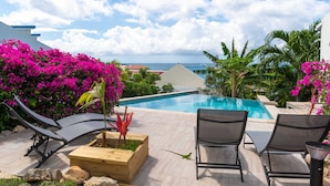 A poolside area with lounge chairs, a wooden planter with flowers, and a view of the ocean. - Blue Sail Apartments - 1 bedroom apartments (sint maarten)