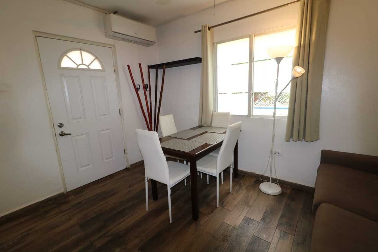 A dining area with a table and chairs, a floor lamp, a window with curtains, and a door with an air conditioning unit.