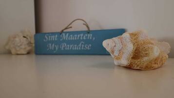 Un letrero azul con el texto "Sint Maarten, My Paradise" y un objeto texturizado que recuerda a una esponja o cojín.
