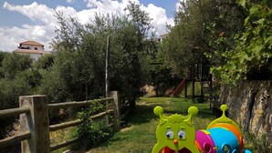 Un parque infantil con tobogán y estructuras para escalar, rodeado de árboles y una valla de madera.