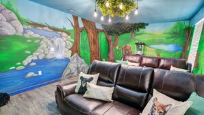 Une pièce décorée d’une fresque représentant une scène de forêt, avec un canapé en cuir agrémenté de coussins et un luminaire suspendu.