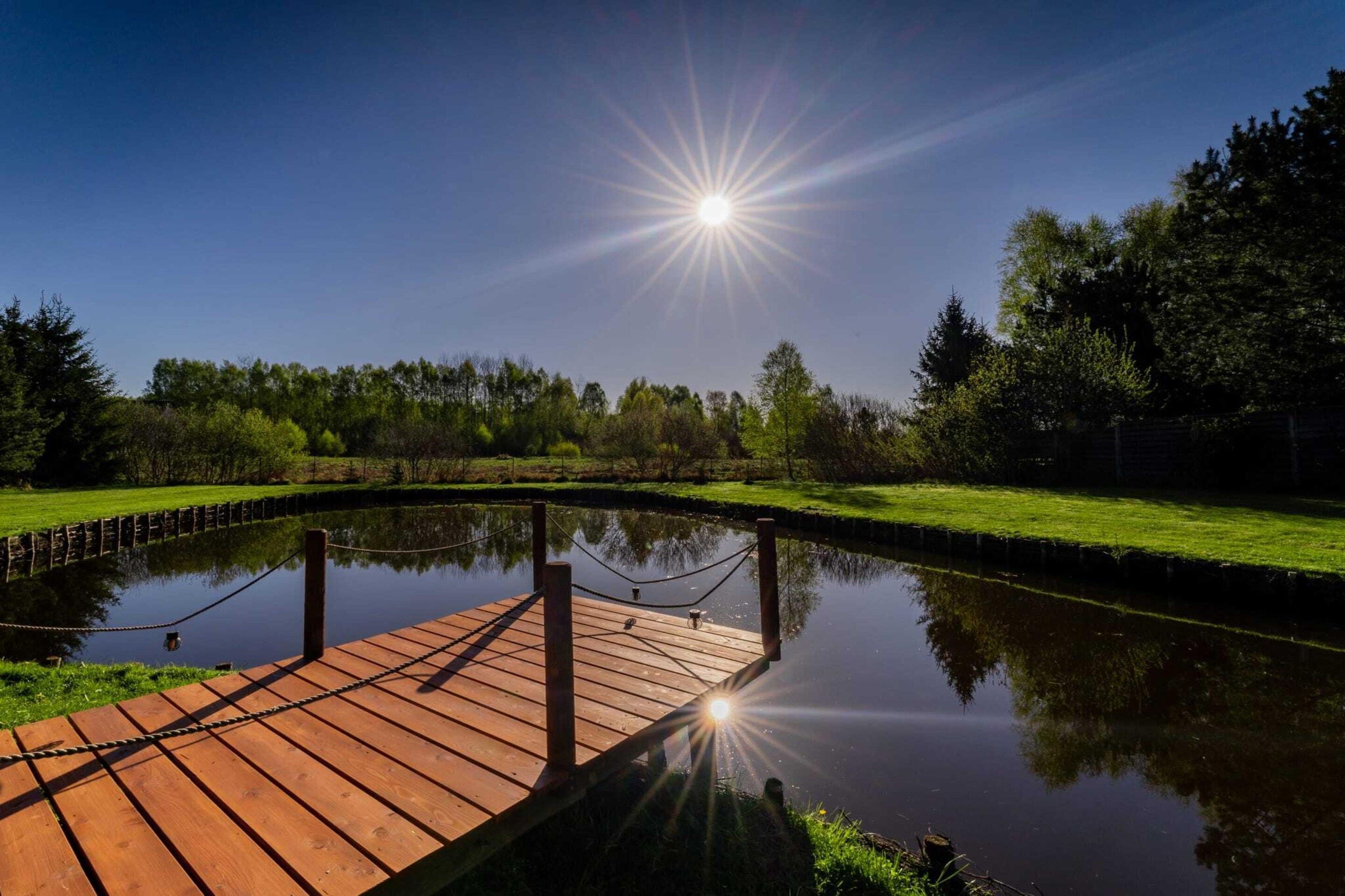 A wooden dock extending over a calm body of water, surrounded by lush greenery and trees.