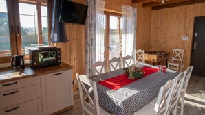 Une cabane en bois comprenant un coin repas, une kitchenette et un téléviseur fixé au mur.