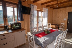 Une cabane en bois comprenant un coin repas, une kitchenette et un téléviseur fixé au mur.