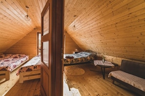 A cozy attic bedroom with wooden walls and a sloped ceiling. There is a bed with a floral bedspread, a small table with a vase, and a sofa. - Holiday Home With Private Pond, Jacuzzi and Sauna (Lipusz)