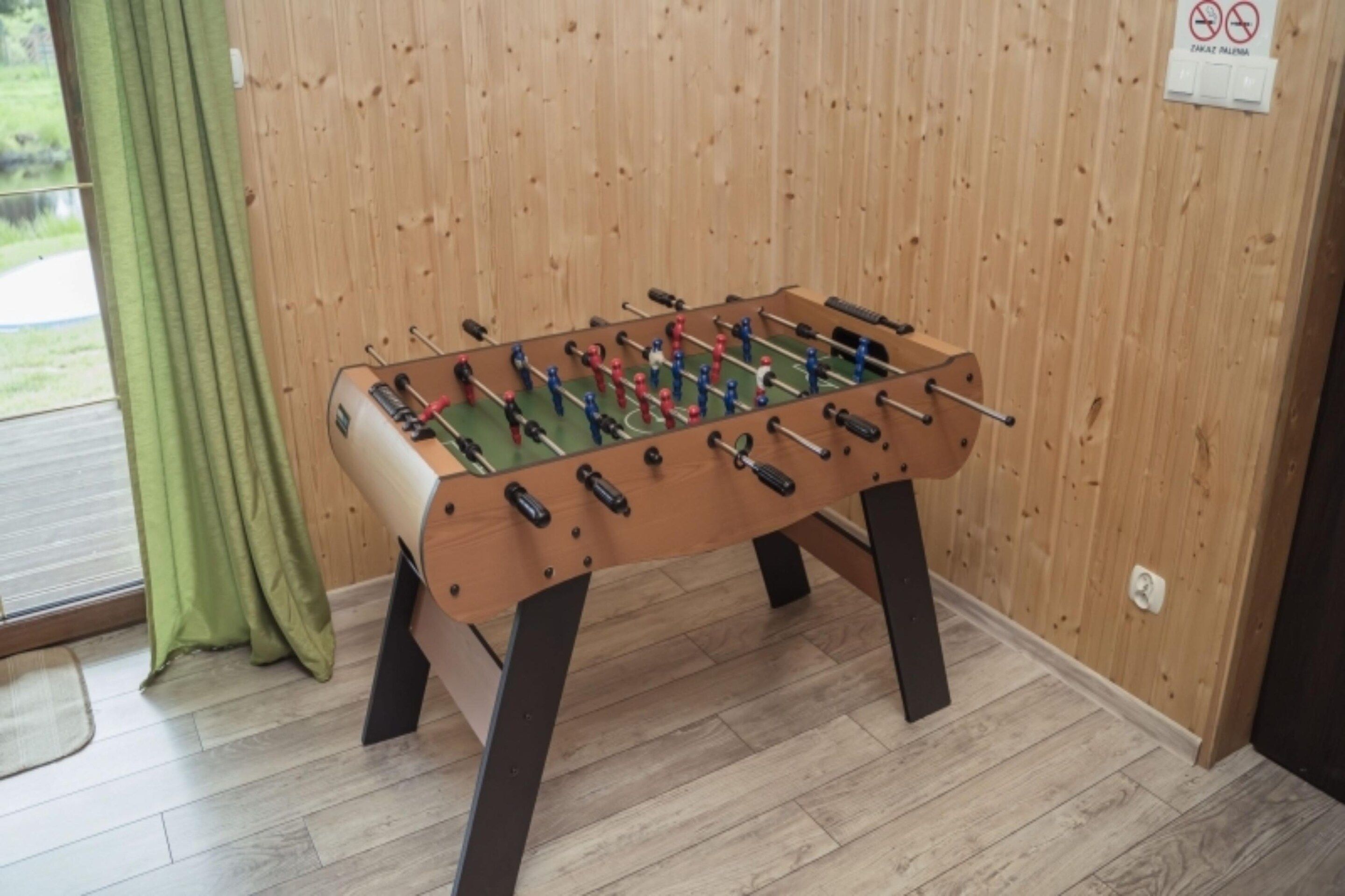 A wooden foosball table in a room with a wooden floor and walls.