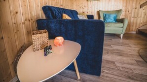 Une pièce avec une table ronde, un canapé bleu et un canapé vert, le tout adossé à des murs en bois.