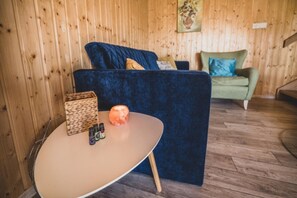 Une pièce avec une table ronde, un canapé bleu et un canapé vert, le tout adossé à des murs en bois.