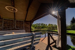 A wooden deck with benches, a brick wall, and a view of a pond and trees. - Holiday Home With Private Pond, Jacuzzi and Sauna (Lipusz)