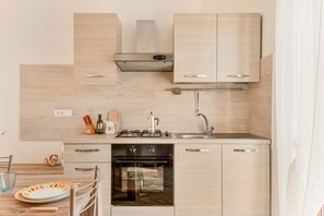 A modern kitchen with light wood cabinetry, a stainless steel range hood, a built-in oven, and a sink.