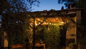 Ein Außenbereich mit Terrasse, Steinböden, Holzbanken und Lichterketten.
