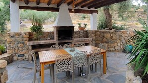 Een terras buiten, met een stenen muur, een houten tafel en metalen stoelen.
