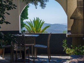 Um terraço ao ar livre com mesa e cadeiras, vista para montanhas e plantas em vasos.