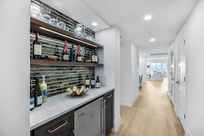 Een moderne keuken met wijnflessen en glazen op planken, een marmeren aanrecht en een houten vloer.