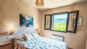 Una camera da letto con un letto, un quadro che raffigura un cervo, due applique, una finestra con vista e un comodino.