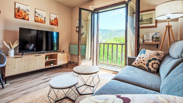 Un soggiorno con televisione, divano, due tavolini e un balcone vista.