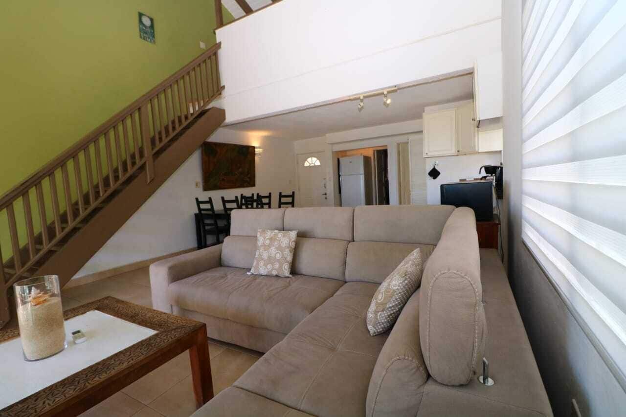 A living room with a beige sofa, a glass coffee table, and a staircase.