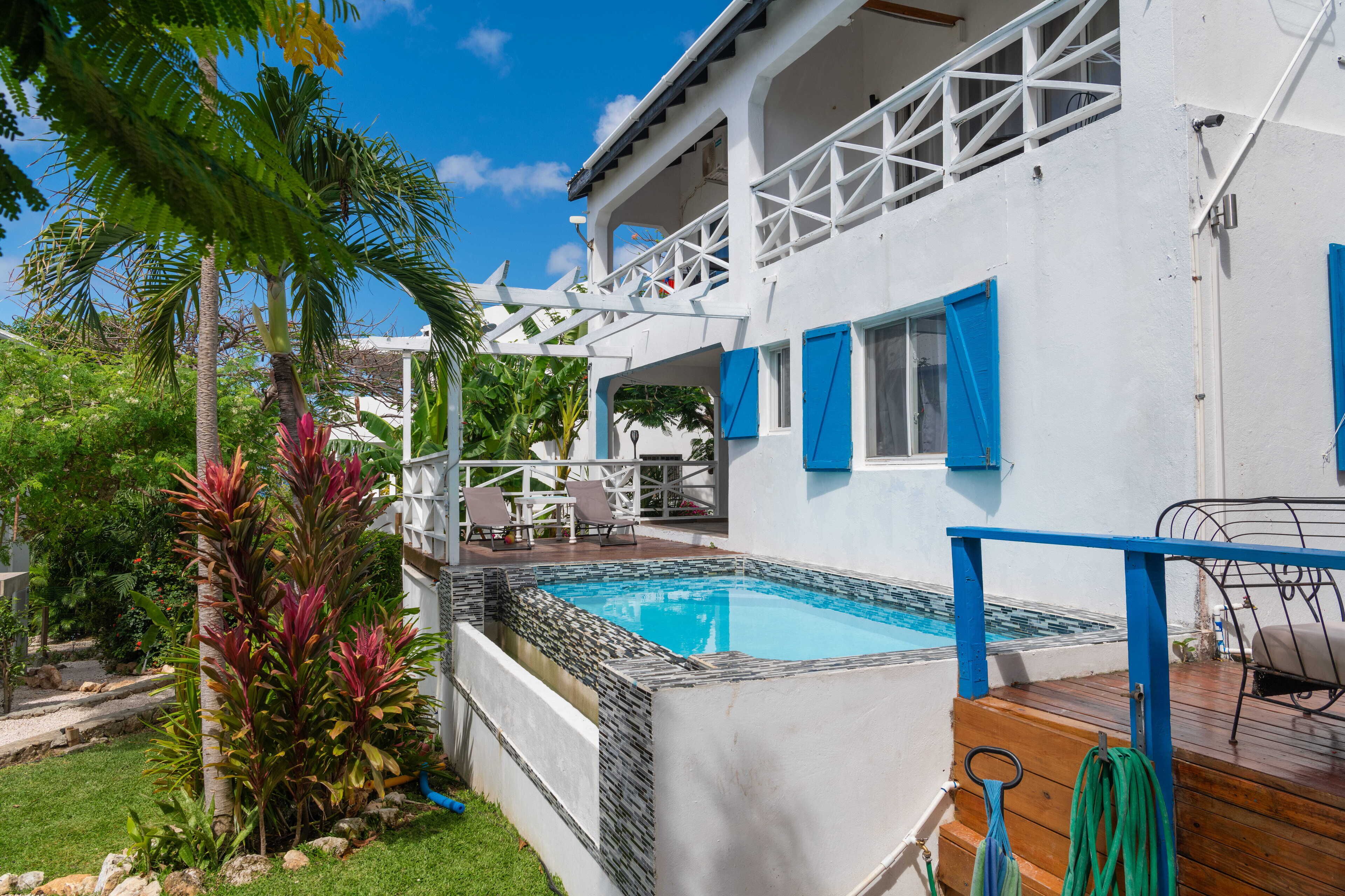 A white house with a pool, blue shutters, and a wooden deck.