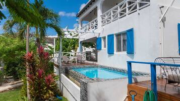 A white house with a pool, blue shutters, and a wooden deck.