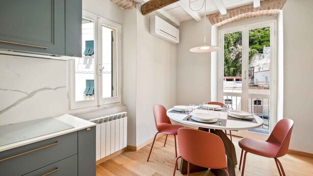 Una cucina moderna con piano di lavoro in marmo, mobili grigi e zona pranzo con tavolo rotondo e sedie rosse.