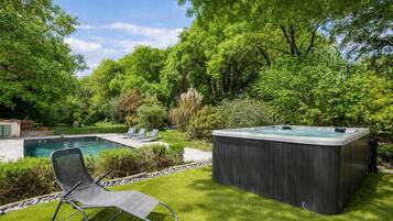 A backyard with a swimming pool, a hot tub, and two lounge chairs.