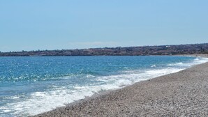 En kyststrand med gruset strand, klart blå hav og en by i det fjerne.