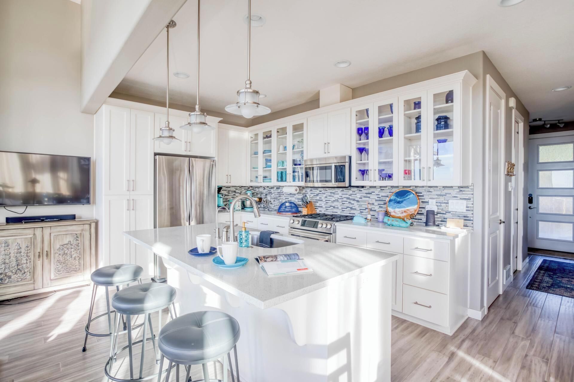 Una cocina moderna con armarios blancos, electrodomésticos de acero inoxidable y una isla central con taburetes de bar.