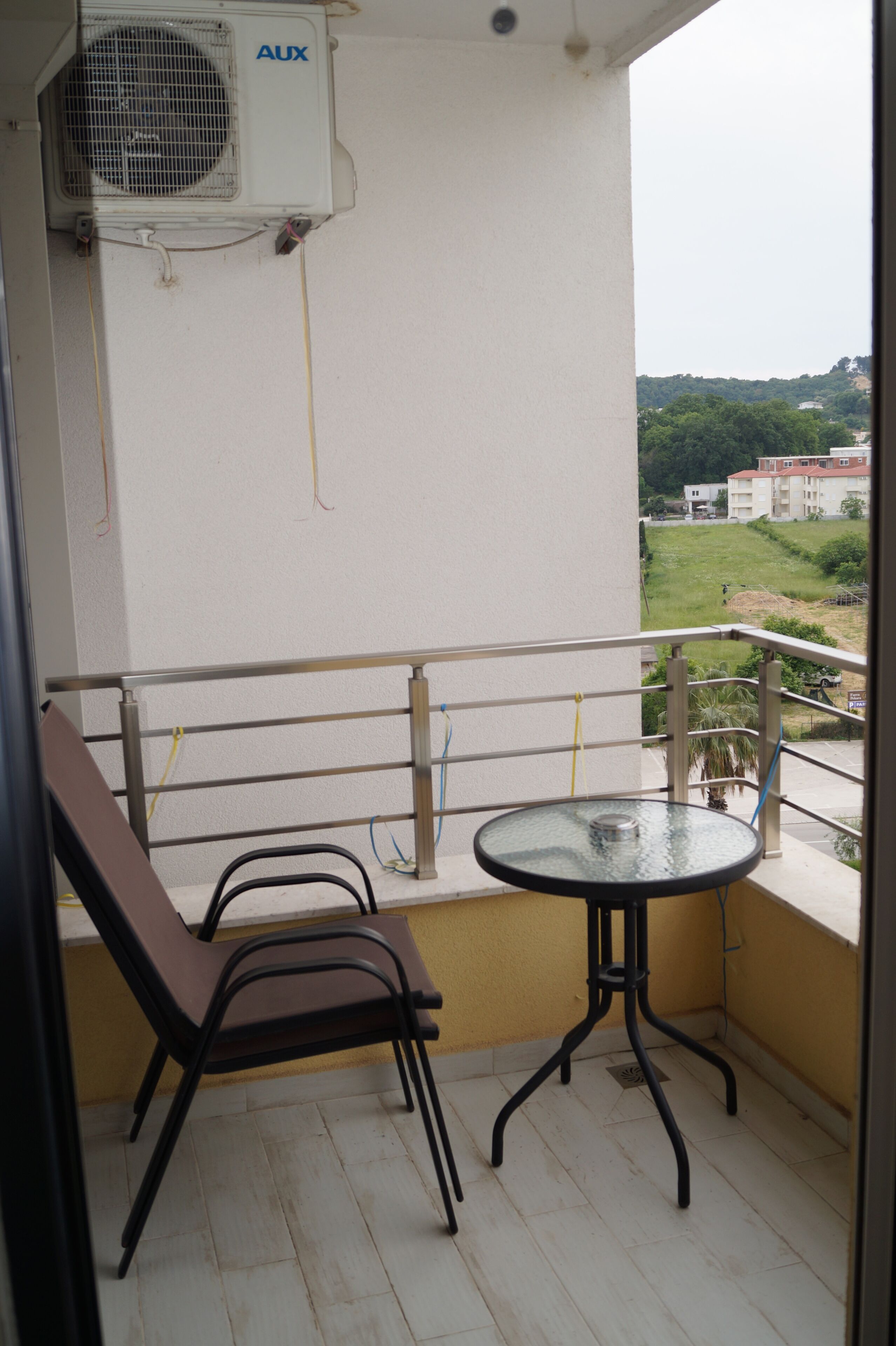Un balcon avec une table et des chaises, un appareil de climatisation et une vue sur un paysage verdoyant.