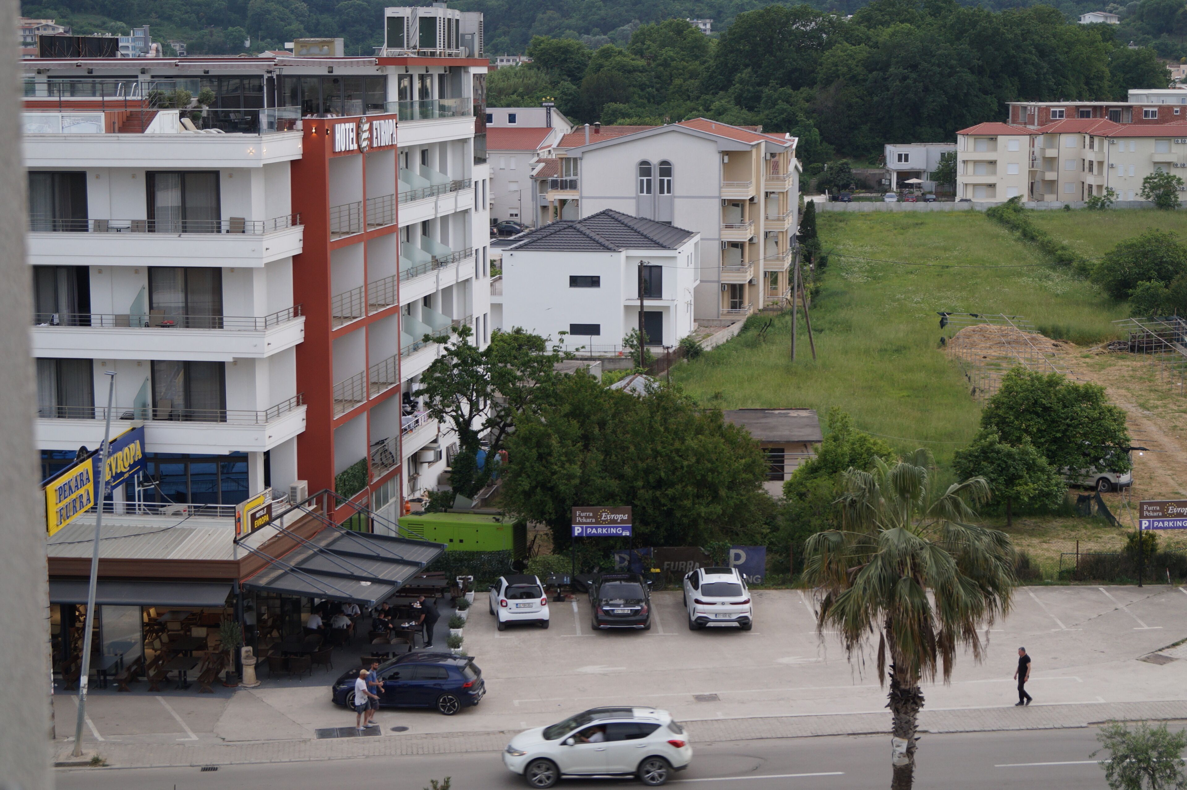 A multi-story hotel with balconies, a parking lot, and a grassy area with a palm tree.