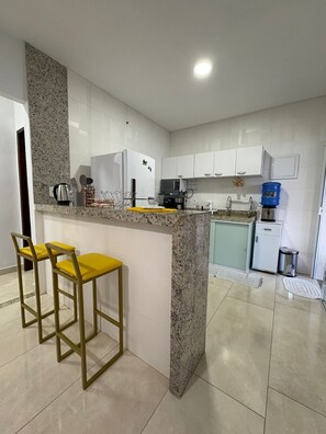 A modern kitchen with white cabinets, a granite countertop, and two yellow bar stools. - Beach house with pool and barbecue - Búzios-RJ La casa Azul (Armação dos Búzios)