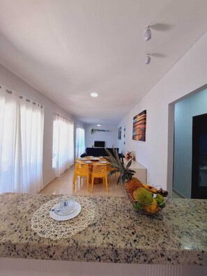 A modern living room with a dining area, a TV, and a large window with curtains. - Beach house with pool and barbecue - Búzios-RJ La casa Azul (Armação dos Búzios)