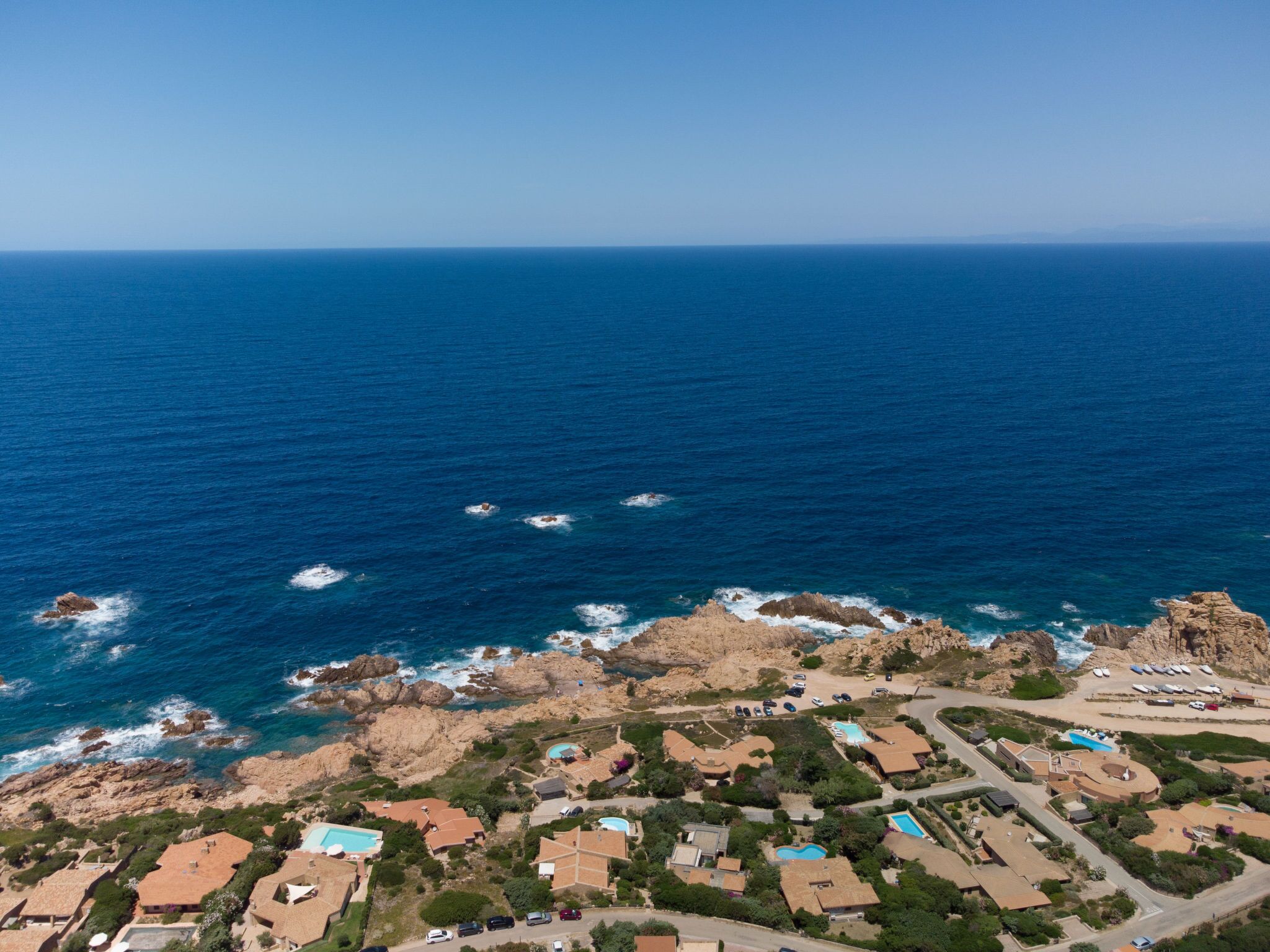 Eine Vogelperspektive eines Küstenresorts mit mehreren Gebäuden, Schwimmbecken und einer felsigen Küstenlinie.