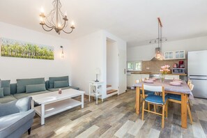 Ein modernes Wohnzimmer mit einer Couch, einem Couchtisch und einem Esstisch. Es gibt eine Küchenzeile mit einem Kühlschrank, einer Mikrowelle und Schränken.