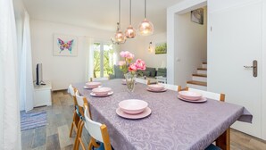 Zona pranzo con un tavolo lungo apparecchiato per quattro persone, un vaso di fiori rosa e una scala che conduce in un'altra stanza.