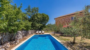 Una piscina con lettini, un muro in pietra e un edificio con tetto in tegole.