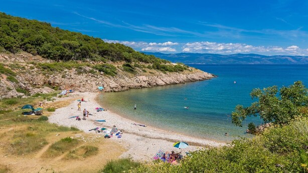 Una spiaggia con acque cristalline, terreno roccioso e vegetazione.