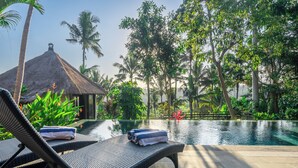 Un espace aménagé au bord de la piscine, avec des chaises longues, une structure à toit de chaume et une végétation tropicale luxuriante.