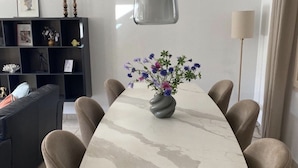 A dining table with a marble top, surrounded by six chairs, in a modern living room with a dark sofa and a bookshelf. - Detached Family Villa in Les Cammazes (Les Cammazes)