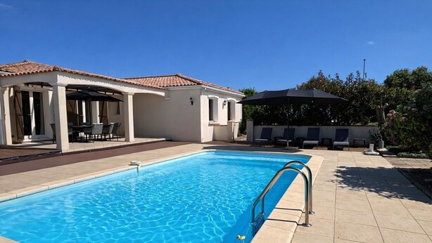 A swimming pool with a tiled deck, a covered seating area, and a building with a tiled roof. - Detached Family Villa in Les Cammazes (Les Cammazes)