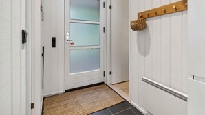 Un pasillo con una puerta de vidrio esmerilado, una cesta tejida sobre un estante de madera y un felpudo con textura.