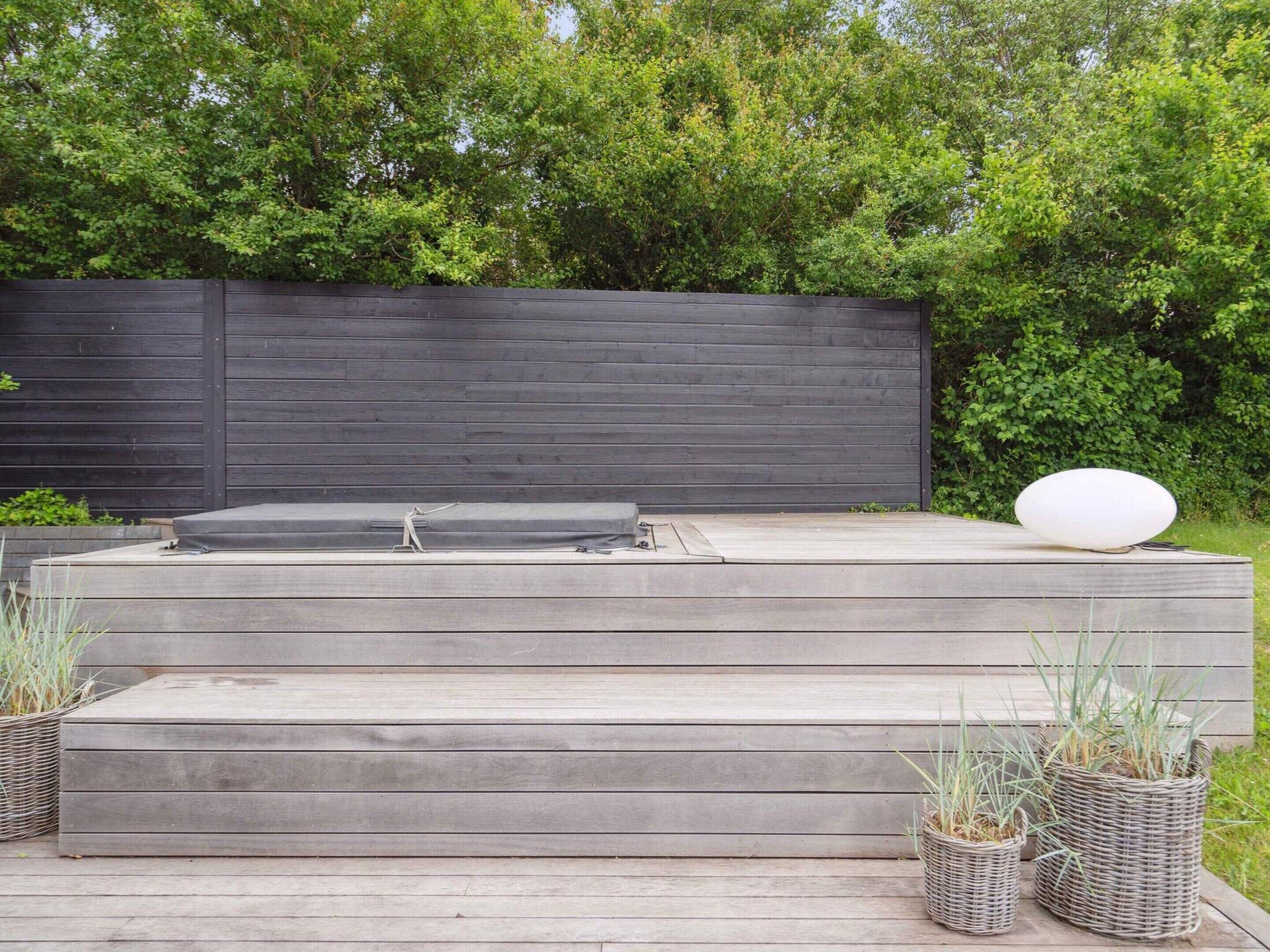 A wooden deck with a built-in hot tub, wicker planters, and a dark fence in the background.