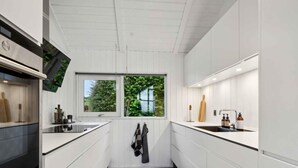Cocina moderna con armarios blancos, encimeras negras y suelo de baldosas negras. Hay una ventana con vistas a la vegetación.