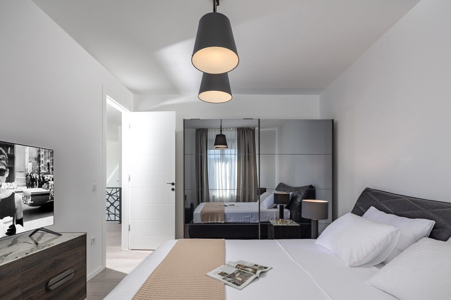 Moderni hotellihuone, jossa on sänky, yöpöytä, lamppu ja suuri peili.