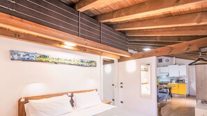 Ein Schlafzimmer mit Bett, Nachttischen, einem Gemälde und Blick in einen Küchenbereich.