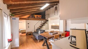 Ein kompakter Wohnraum mit Holzboden, einer Treppe, einer Couch, einem Esstisch und einer Küchenzeile.