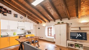 Eine gemütliche Küche mit Holzbalken, einer Essecke mit Tisch und Stühlen sowie einem Fernseher auf einem Regal.